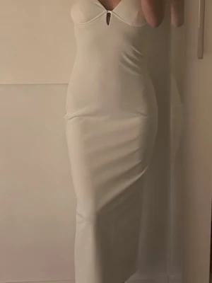 Vit långklänning med bygel och slimmad passform - Säljer en elegant vit långklänning från Bershka med bygel i kuporna och smala axelband. Klänningen har en slimmad passform och ett litet nyckelhål vid bysten. Oanvänd klänning med prislapp ord pris 35€ säljs 249:-