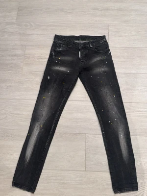 Svarta Dsquared2 skinny jeans med färg - Svarta jeans från Dsquared2 med skinny passform och färg vitt och gult . Jeansen har klassiska slitna detaljer och en snygg look. Lite liten i storlek.