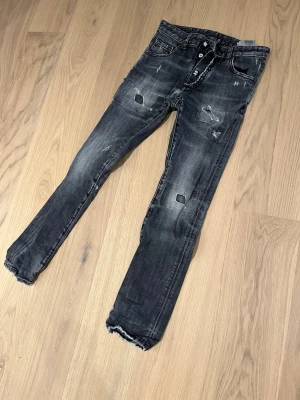 Svarta skinny jeans från Dsquared2 - Säljer ett par svarta skinny jeans från Dsquared2 med slitna detaljer. Jeansen har en mörk tvätt med grå toner. Perfekt för dig som gillar en smal passform och streetstil. Passar bäst till 12 åringar som är ungefär 152 cm långa. 