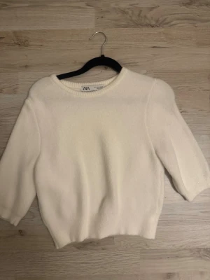 Vit stickad tröja från Zara - Mysig vit stickad tröja från Zara med rund halsringning och trekvartsärm. Perfekt till både jeans och kjol för en clean och enkel look. Materialet känns mjukt och tröjan har en clean look.