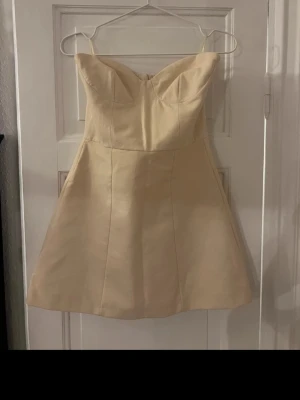 Champagnefärgad kort klänning från Zara - Säljer en snygg champagnefärgad kort klänning från Zara i storlek XS. Klänningen har axelband, markerad byst och en lätt utsvängd kjol. Materialet är mjukt och känns lyxigt, perfekt för dig som vill ha en stilren look. Dragkedja i ryggen för enkel påklädning.