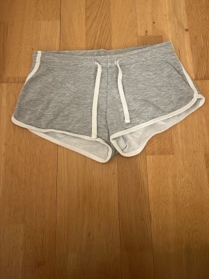 Grå mjuka shorts från Sister XS - Superbekväma grå shorts från Sister i storlek XS. De har vit kant runtom och snörning i midjan för perfekt passform. Perfekta för chill dagar eller träning. Klassisk sportig look med loose fit.