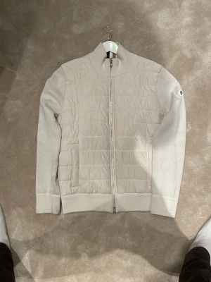 BOSS cardigan  - Snygg beige cardigan från BOSS med quiltad framsida och ribbad krage. Jackan har hel dragkedja och en diskret BOSS-logga på ärmen. Materialmix med polyester och bomull, perfekt för dig som gillar stilren design. Riktigt snygg och väldigt få som har, knappt använd! Stl L passar även M