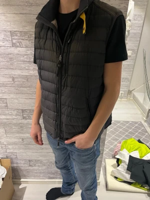 Svart dunväst från Parajumpers - Säljer en svart dunväst från Parajumpers i storlek XL. Västen har quiltad design, två dragkedjefickor och en gul detalj vid kragen. Insidan är ljusgrå och materialet är lätt och syntetiskt. Perfekt att slänga över en hoodie eller t-shirt. Men liten i storleken skulle jag säga. Dragkedjan är lite trög men går att stänga☺️