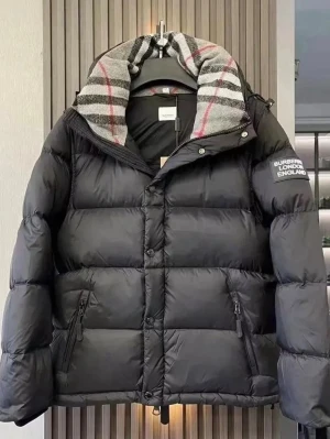 Svart pufferjacka från Burberry - Säljer en svart pufferjacka från Burberry med rutigt foder i grått, vitt och rött. Jackan har huva, dragkedja och knappar framtill samt två fickor med dragkedja. Perfekt för kalla dagar och har en cool Burberry patch på ärmen.