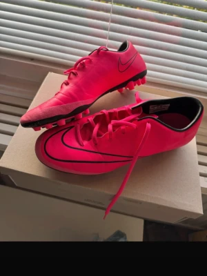 Nike Mercurial rosa fotbollsskor - Säljer ett par Nike Mercurial fotbollsskor i stark rosa färg med svarta detaljer. Utsidan är i syntetmaterial och insidan har svart kant. Perfekt för dig som vill sticka ut på planen. 