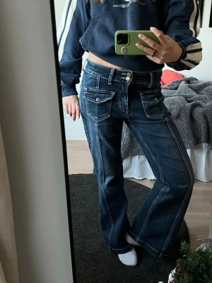Mörkblå vida jeans med coola fickor - Mörkblå jeans med vida ben och coola fickor framtill med silverknappar💙💙 Jeansen har låg midja och kontrastsömmar samt två knappar. Köpta i Italien och är väldigt sköna i materialet då de är gjorda av bomull, polyester och elastan!