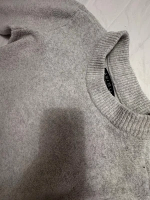 Ljusgrå stickad tröja från Amisu - Mysig ljusgrå stickad tröja från Amisu med rund halsringning och breda ribbade muddar vid ärmslut och hals. Perfekt för kyliga dagar och enkel att matcha med jeans eller kjol.