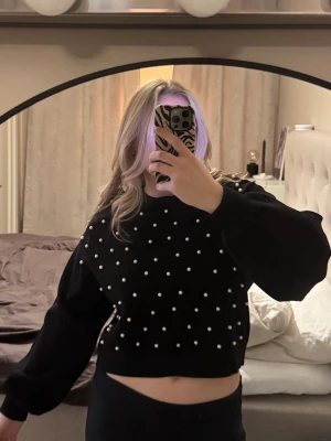Svart croppad stickad tröja Zara - Säljer en svart croppad stickad tröja från Zara med pärldetaljer över hela framsidan. Tröjan har lång ärm och en loose passform. Perfekt för dig som vill ha något extra till din outfit.
