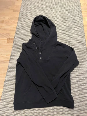 Svart hoodie, These Glory Days - Svart hoodie med snygg knappstängning vid halsen och stor huva. Tröjan har långa ärmar, känguruficka framtill.