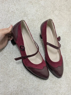 Vinröda Mary Jane pumps med mockadetaljer - Oanvända, bekväma, 38.5 med dämpad sula 🍓🌹                                             Säljer ett par vinröda Mary Jane pumps med spetsig tå och låg klack. Skorna har snygga detaljer i både mocka och skinn, samt ett dekorativt spänne och rem över foten. Perfekt för dig som gillar retrovibbar och vill sticka ut med en unik look.