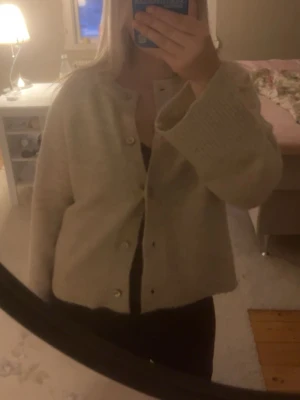 Beige kofta från Gina Tricot - Supermysig beige kofta från Gina Tricot med rund hals och pärlemorknappar. Koftan är stickad och har långa ärmar samt ribbade muddar. Perfekt att slänga på sig när det är lite kyligare ute.