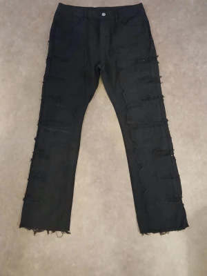 Svarta jeansbyxor med råa kanter från Temu.  - Säljer ett par svarta jeansbyxor i storlek L från Temu med råa, fransiga kanter nertill och slitna detaljer längs benen. Byxorna har en rak passform och är tillverkade i en mix av bomull, polyester och spandex för lite stretch. Perfekta för dig som gillar en edgy och avslappnad stil.