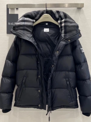 Svart pufferjacka från Burberry - Svart pufferjacka från Burberry med avtagbara ärmar, så den kan användas som väst. Jackan har en stor huva med grått och svart rutigt foder, dragkedja och knappar framtill samt två snedställda fickor med dragkedja. Perfekt för kalla dagar och riktigt snygg streetstil. Finns i båda storlek M och S.