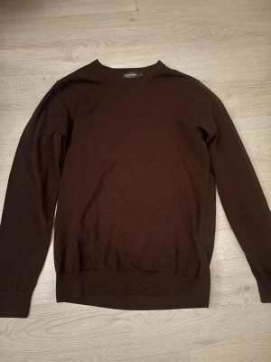 Brun tröja i bomull från Dressmann - Mörkbrun långärmad tröja från Dressmann i Supima bomull. Enkel och stilren design med rund halsringning och ribbade muddar vid ärmslut och nederkant. Perfekt för dig som gillar klassiska plagg med en clean look.