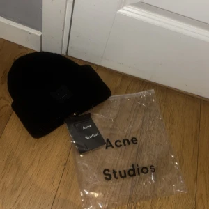  mössa Acne Studios - Säljer en svart ribbstickad mössa från Acne Studios med den klassiska ansiktsloggan framtill. Mössan är i mjukt material och har en bred uppvikt kant. 
