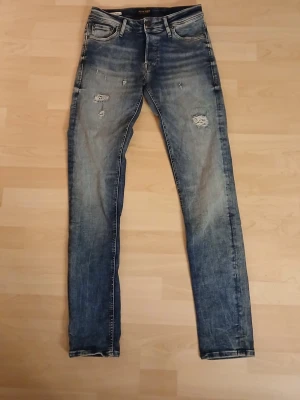 Jack & Jones Slim Fit Glenn jeans W 31 L 34 - Säljer ett par blå slim fit jeans från Jack & Jones, modell Glenn. Jeansen har slitna detaljer och hål på framsidan för en cool, avslappnad look. Klassisk femficksmodell med normal midja och smal passform. Tillverkade i tåligt denimtyg.