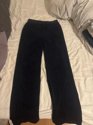 Juicy Couture byxor - Säljer mina mörkblå mjukisbyxor från Juicy Couture i storlek S. Byxorna har bred resår i midjan, raka ben och fickor både fram och bak med knappdetaljer. Tyget runt ena knappen där bak har lossnat men inget man lägger märke till på håll. 