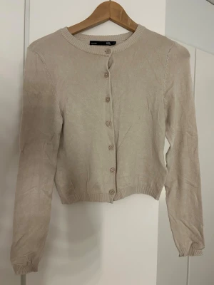 Beige kofta från 157, XS - Säljer en enkel och stilren beige kofta från 157 i storlek XS. Koftan har rund halsringning, långa ärmar och knappar framtill. Materialet är mjukt och stickat, perfekt för lager på lager under höst och vår. 