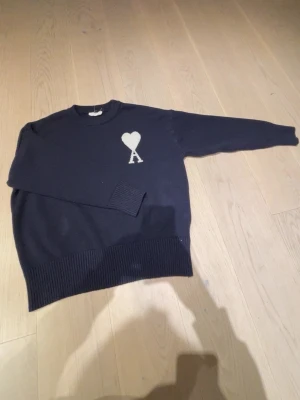 Mörkblå stickad tröja från Ami Paris  - Säljer en mörkblå stickad tröja från Ami Paris med ikoniskt hjärta och A på bröstet i vitt. Tröjan har rund hals, ribbade muddar och är långärmad. Perfekt för dig som vill ha en clean men ändå statement look. Ställ gärna frågor                                    Priset kan diskuteras 