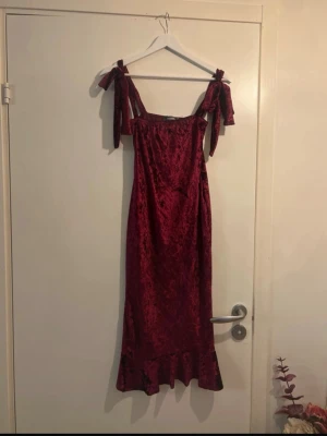 Vinröd sammetsklänning Missguided - Supersnygg vinröd långklänning från Missguided i mjuk sammet. Klänningen har knytband på axlarna, volangkant nertill och en figurnära passform. Perfekt för dig som vill sticka ut med en lyxig känsla och trendig look.