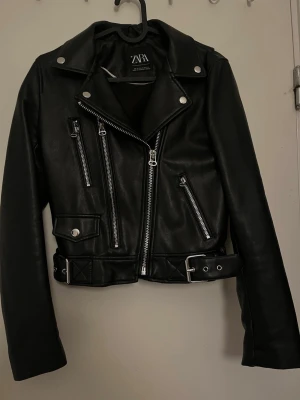 Zara bikerjacka skinnimitation strl XS - Säljer denna snygga bikerjackan från Zara i läderimitation! Dock så har den en liten spricka där uppe (se bild) som man inte tänker så mycket på annars i fint skick.  