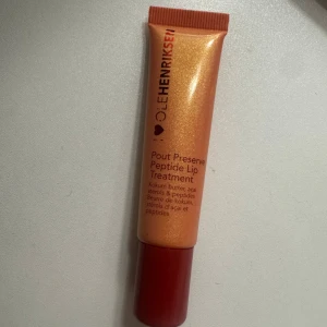 OLEHENRIKSEN Pout Preserve Lip Treatment - Peptide Lip Treatment från OLEHENRIKSEN i en skimrande orange tub med röd kork. Innehåller kokumsmör, açaísteroler och peptider för att vårda och återfukta läpparna. Perfekt att ha i väskan för mjuka och återfuktade läppar.
