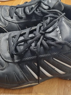 Svarta sneakers från Pan, strl 45 - Svarta sneakers från Pan med vita detaljer på sidorna och klassisk snörning. Skorna har en sportig look med rund tå och platt sula. Tillverkade i syntetmaterial och textilfoder för extra komfort. Perfekta för dig som gillar enkel och stilren design.