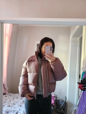 Ljusrosa dunjacka från Adidas - Säljer en snygg ljusrosa pufferjacka från Adidas i storlek 38. Jackan är dunfylld (80/20) och har en klassisk pufferlook med hög krage och dragkedja framtill. Perfekt för kalla dagar och riktigt skön att bära. Adidaslogga på insidan. I nyskick då den blev använd en gång bara.