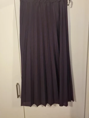 Mörklila plisserad långkjol - Säljer en mörklila plisserad långkjol med bred resår i midjan. Kjolen har ett snyggt fall och är perfekt för dig som gillar en stilren och enkel look. Materialet känns lätt och flowy, vilket gör den superbekväm att bära. Den är hemsytt. 