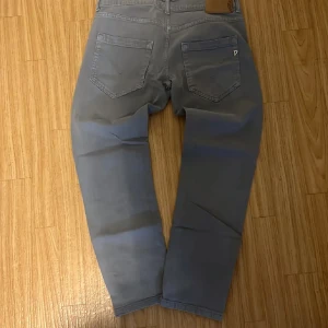Grå jeansbyxor från Dondup  - Snygga grå jeansbyxor från Dondup med klassisk femficksdesign och diskret dondup l-logga på bakfickan. Byxorna har rak passform och är tillverkade i mjukt bomullsmaterial. Perfekta för en avslappnad och stilren look.
