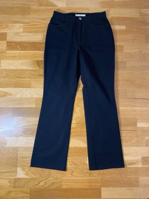 Svarta bootcut byxor från MAC - Svarta byxor från MAC i modellen Melanie. Byxorna har bootcut passform, klassiska fickor både fram och bak samt bälteshällor. Materialet är mjukt och stretchigt med 93% bomull och 7% elastan. Perfekta för en clean och stilren look.