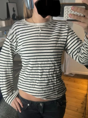 Randig långärmad topp från Zara - Säljer en klassisk långärmad topp från Zara i vitt med svarta horisontella ränder. Toppen har rund halsringning och är i ett mjukt bomullsmaterial. Perfekt till jeans eller kjol för en enkel och stilren look.