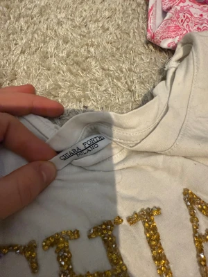 Vit t-shirt med guldpaljetter Chiara Forthi - Snygg vit t-shirt från Chiara Forthi Milano med korta ärmar och stor CHIARA-text framtill i glittrande guldpaljetter. Mjuk och skön bomullskvalitet, perfekt för dig som gillar att sticka ut med detaljer.