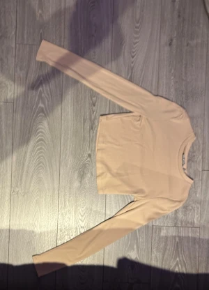 Beige långärmad topp - En stilren beige långärmad topp med rund halsringning. Modellen är enkel och passar perfekt till jeans eller kjol. Tunn och mjuk i materialet, vilket gör den skön att bära under flera säsonger.