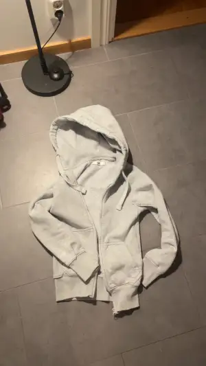 Säljer en ljusgrå hoodie från Russemerch i storlek XXS. Den har dragkedja, två fickor fram och en stor huva med dragsnören. Insidan är mjukt fodrad för extra komfort. Perfekt för dig som gillar en enkel och clean stil.