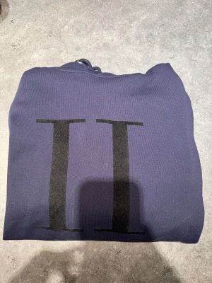 Mörkblå hoodie från Les Deux - Säljer en mörkblå hoodie från Les Deux i modellen Encore. Tröjan har en stor svart II-logga på bröstet, huva med snörning och är tillverkad i mjuk bomull. Nyskick, aldrig använd. Storlek S och sitter som en storlek S. Nypris 1500 kr.