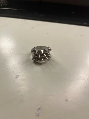 Silvrig ring med nitar från Edblad storlek 19,50mm - Cool och chunky ring i silverfärgat rostfritt stål från Edblad. Rektangulär front med flera små, spetsiga nitar som ger en edgy vibe. Perfekt för dig som gillar statement-smycken och vill sticka ut med din stil. Sälj pga för stor storlek för mig och har köpt en ny storlek.