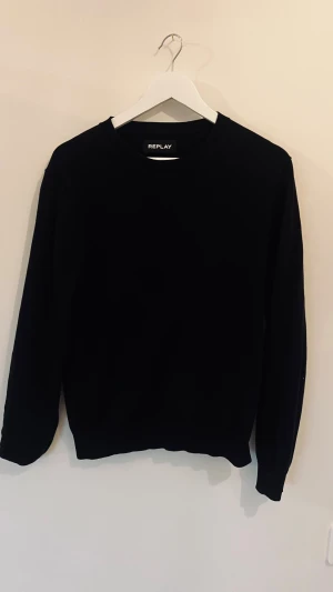 Svart stickad tröja från Replay S/XS - Svart stickad tröja från Replay i klassisk modell med rund hals och långa ärmar. Tröjan har en diskret etikett på sidan med Replay-tryck och är gjord i mjukt material som känns skönt mot huden. Perfekt för dig som gillar stilrena och enkla plagg.