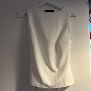 Vit ärmlös topp med öppen rygg Bik Bok - Säljer en stilren vit topp från Bik Bok i storlek S. Toppen är ärmlös med rund halsringning och har en snygg öppen rygg med knytband. Perfekt för dig som gillar minimalistisk och trendig stil. Helt ny endast provad. 