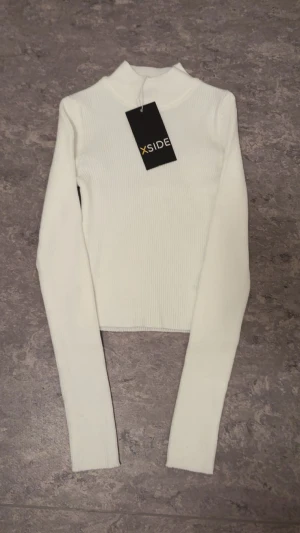 Vit ribbad polotopp  - Säljer en stilren vit polotopp med ribbad struktur. Toppen har lång ärm och en hög krage som ger en clean look. Perfekt att styla med jeans eller kjol för en trendig outfit.