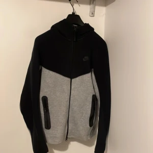 Nike hoodie svart och grå S - Nike hoodie i svart och grått med hel dragkedja och huva. Tröjan har två fickor med dragkedja på framsidan och en stilren design med svart övre del och grå nedre del. Perfekt för chill eller träning, mjukt material och långärmad. Pris går och diskutera