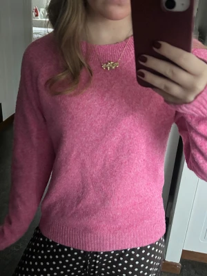 Rosa stickad tröja från Vero Moda - Mysig rosa stickad tröja från Vero Moda i storlek S. Tröjan har rund halsringning, ribbade muddar och långärmade ärmar. Perfekt för dig som gillar färg och vill ha en enkel, skön tröja till garderoben.