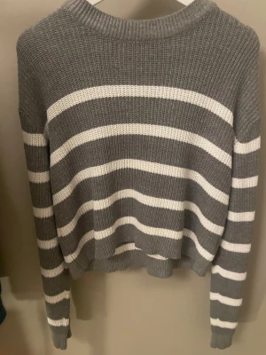 Gråvit randig stickad tröja H&M XS - Säljer en chill stickad tröja från H&M i storlek XS. Den är grå med vita ränder och har en ribbad rund hals. Tröjan är långärmad och har en loose passform, perfekt för att mysa i under hösten och vintern. Materialet är mjukt och känns skönt mot huden.💖💖