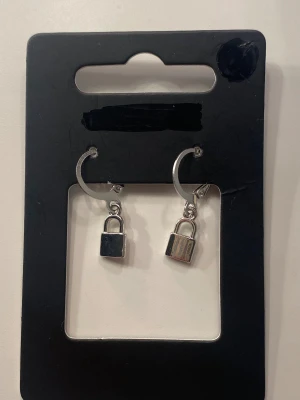 Silvriga örhängen med hänglås - Ett par coola örhängen i silverfärgad metall med små hänglås som berlocker. Runda hoops med låsdetalj som ger en edgy vibe. Helt oanvända ej äkta silver ❤️