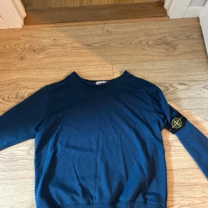 Blå Stone Island sweatshirt - Snygg marinblå sweatshirt från Stone Island med klassisk patch på vänster ärm. Tröjan har rund halsringning och långa ärmar. Tillverkad i mjuk bomull som är skön att ha på sig. Perfekt för dig som gillar streetwear och vill ha en stilren look. lite stor i kragen