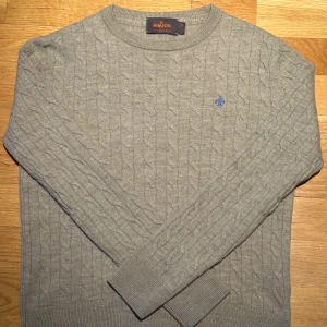 Beige kabelstickad tröja Morris XS - Kabelstickad beige tröja från Morris i 100% merinoull. Rund halsringning och långärmad modell med blå broderad logga på bröstet. Tröjan har ribbade muddar vid ärmslut och nederkant för extra komfort. Perfekt för dig som gillar klassisk stil. Knappt använd. Ordinarie pris 1200kr, säljs för endast 699kr. Passar XXS. Passar alla mellan 140-150 cm