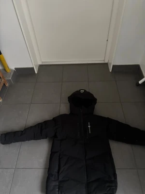 Sail racing jacka - Säljer en svart lång dunjacka från Peak Performance med huva och dragkedja framtill. Jackan är fodrad med Allied Feather + Down 500 fill power och har en clean design med diskret logga på bröstet. Perfekt för kalla vinterdagar och har långa ärmar.