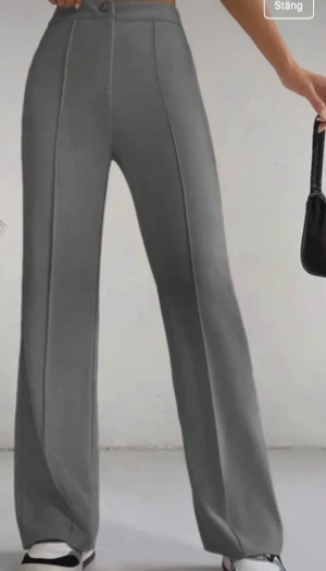 Grå wide kostymbyxor med pressveck - Snygga grå kostymbyxor med wide fit och pressveck längs benen. Byxorna har hög midja, knapp och dragkedja framtill samt raka ben med lite utsvängd siluett. Perfekta för en clean och stilren look. Materialet känns mjukt och har en stretch. Använda 1 gång så är som nya, inget att anmärka. Storlek L men kan passa ev M också beroende på hur tight man vill ha dom runt rumpa/mage. Djur och rökfritt hem