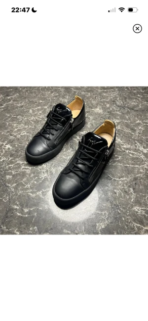 Giuseppe Zanotti  - Snygga svarta sneakers i skinn med matta och blanka detaljer. Skorna har snörning framtill och dragkedjor på sidorna för en cool look. Insidan är beige och sulan är svart. Perfekta för dig som gillar stilrena men ändå unika skor. Skick 9,5-10